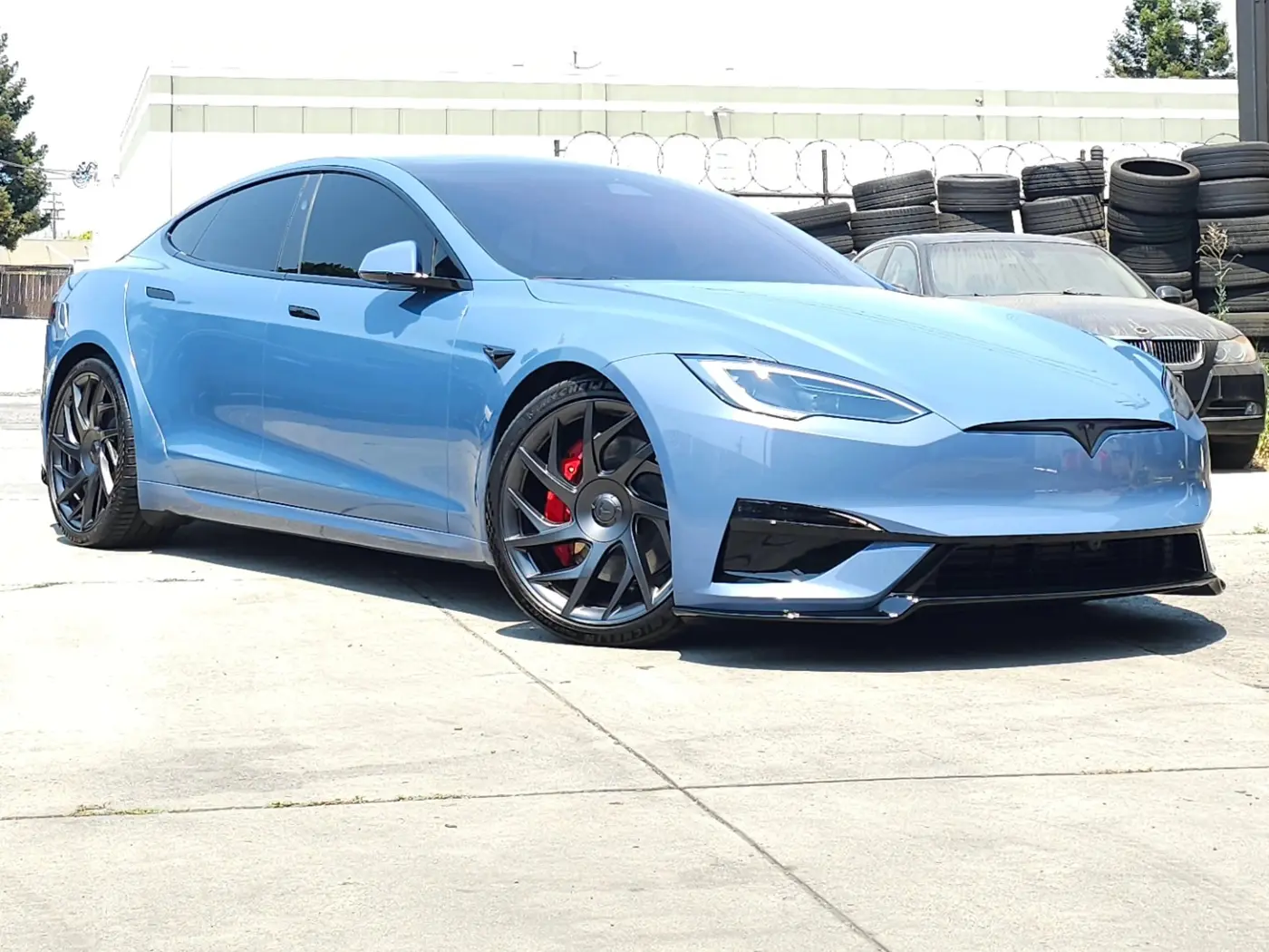 Light-blue Tesla Model S Plaid with red brake calipers and dark wheels, parked on concrete