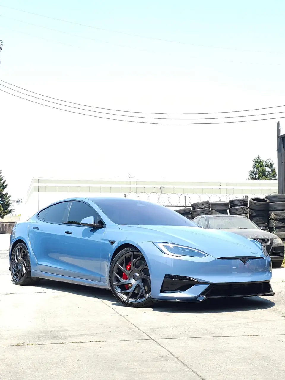 Light-blue Tesla Model S Plaid with red brake calipers behind dark wheels
